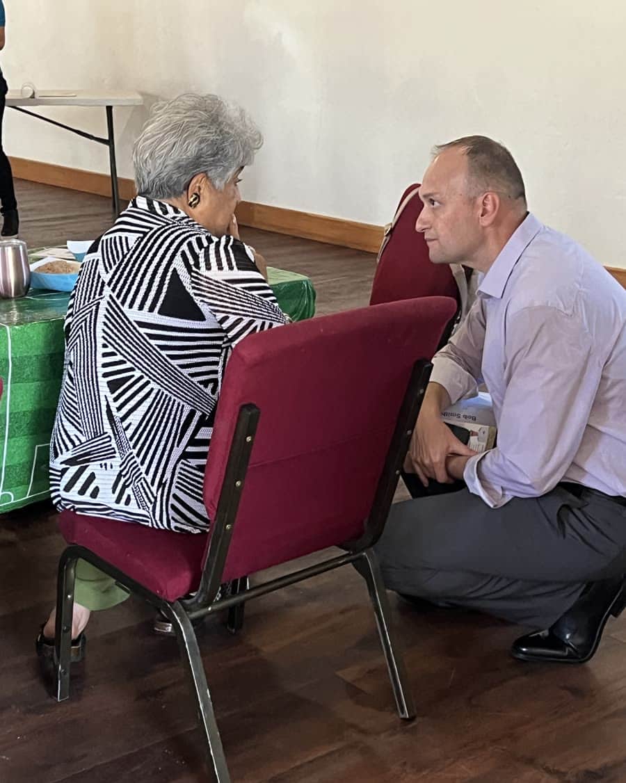 Bob Smith crouching to talk with a seated resident at a community lunch