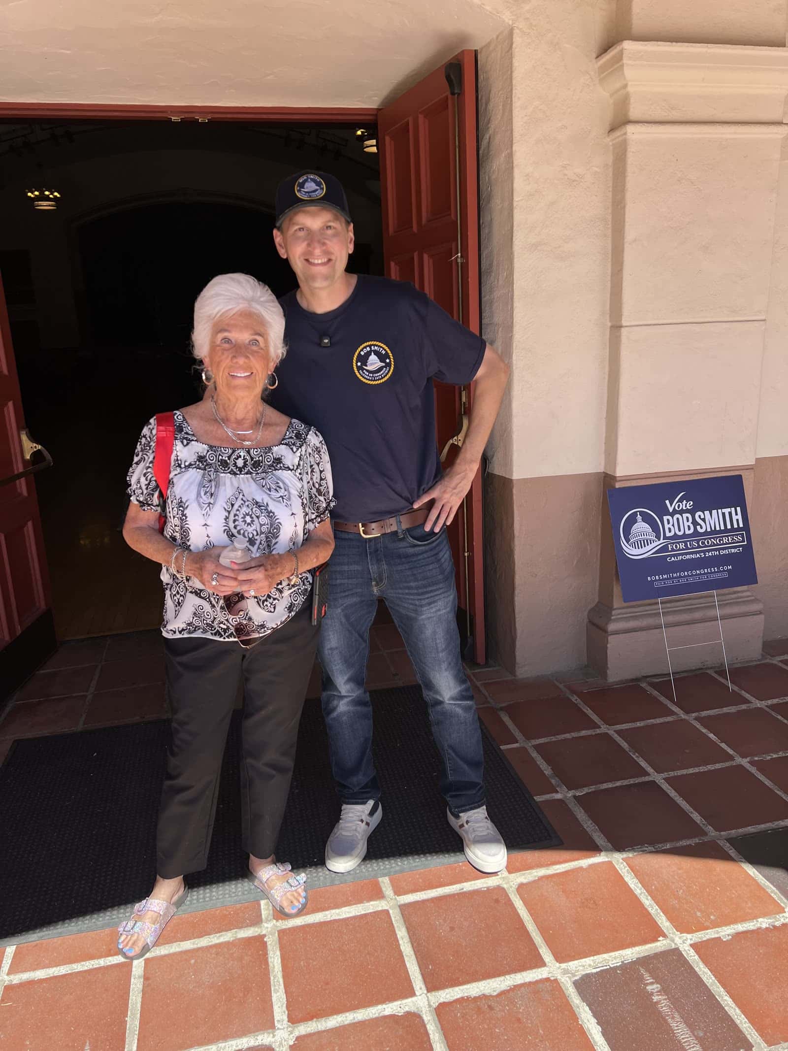 Bob Smith con una asistente afuera de la reunion comunitaria en Orcutt, junto a un letrero de Vote Bob Smith