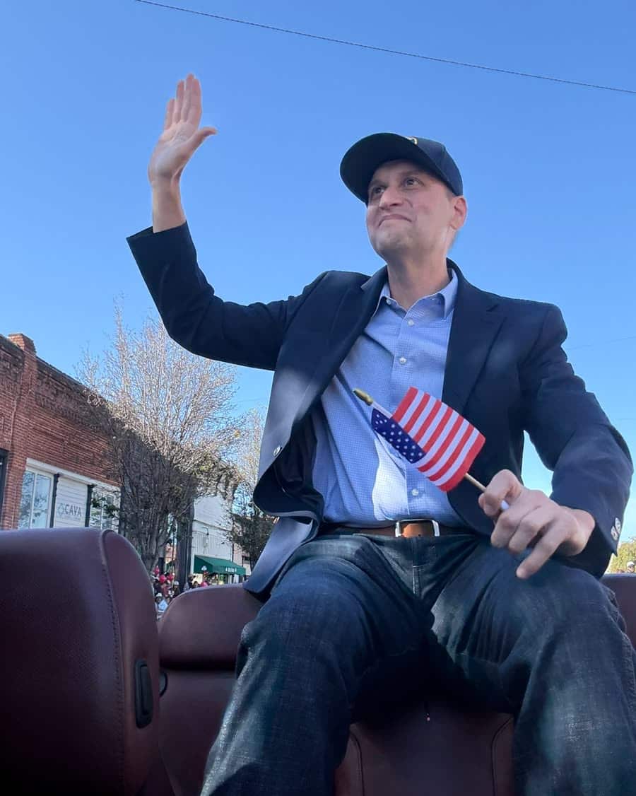 Bob Smith waving from a parade car on a Central Coast main street, holding a small American flag