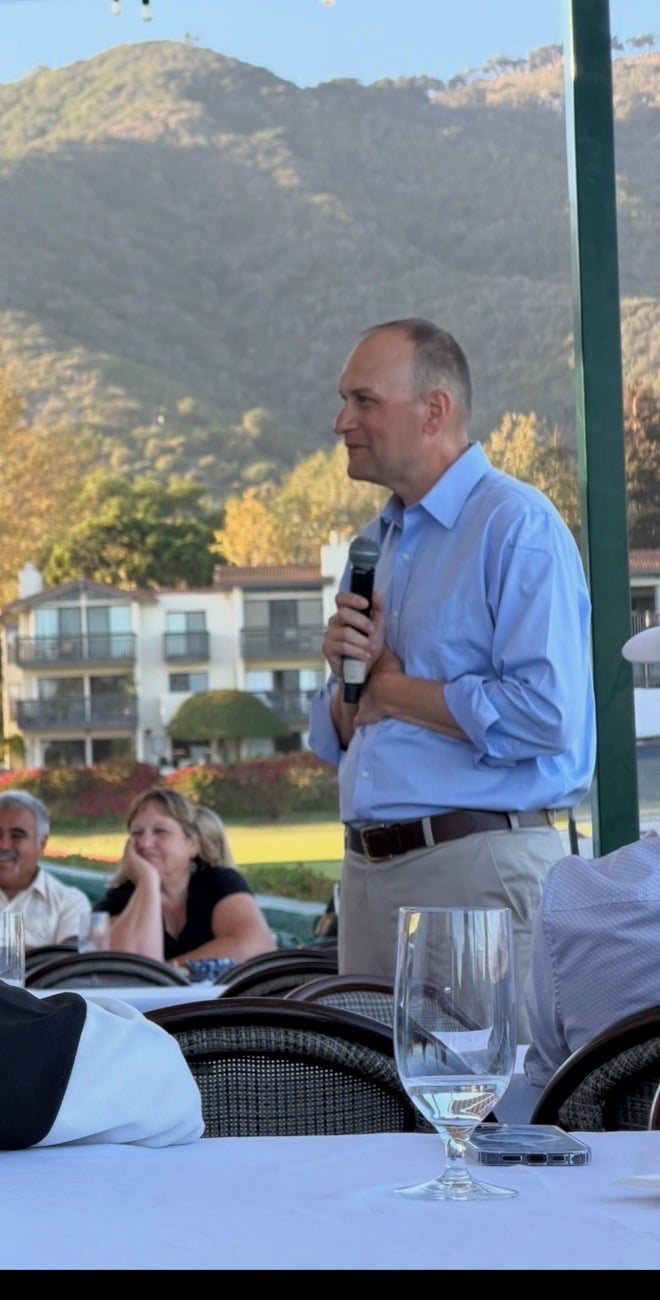Bob Smith speaking into a microphone to seated supporters outdoors at sunset